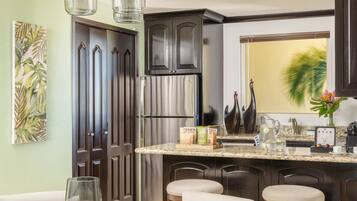 Una cocina moderna con armarios de madera oscura, un refrigerador de acero inoxidable y una mesa de comedor de vidrio con sillas blancas.