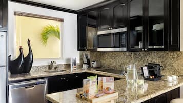 Cocina moderna con armarios oscuros, encimera de granito, lavavajillas, cafetera y una ventana con una planta.