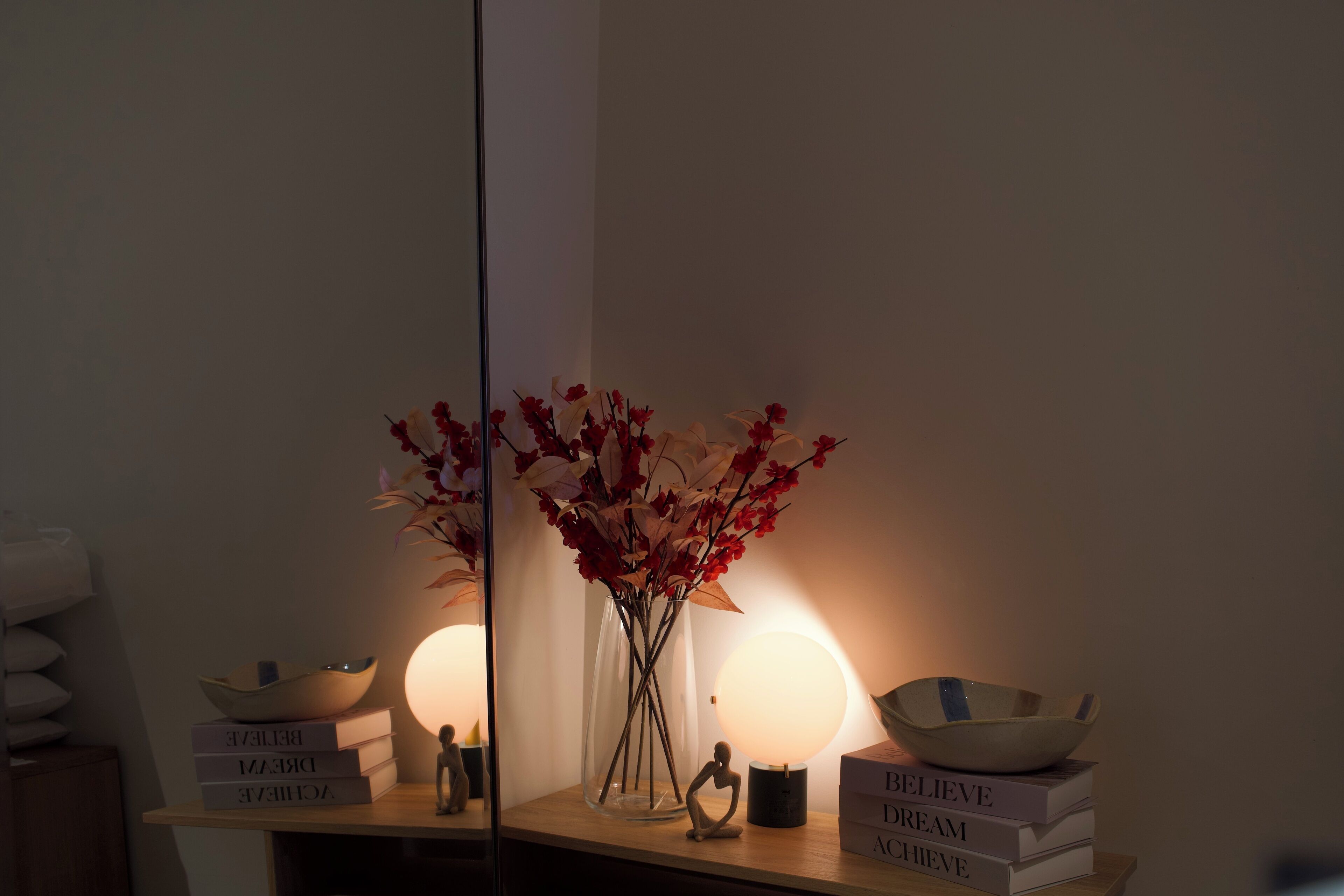 A bedside table with a vase of flowers, a bowl, and a stack of books.