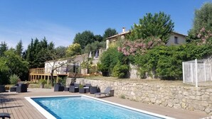 A swimming pool with lounge chairs, a stone wall, and a house with a balcony.