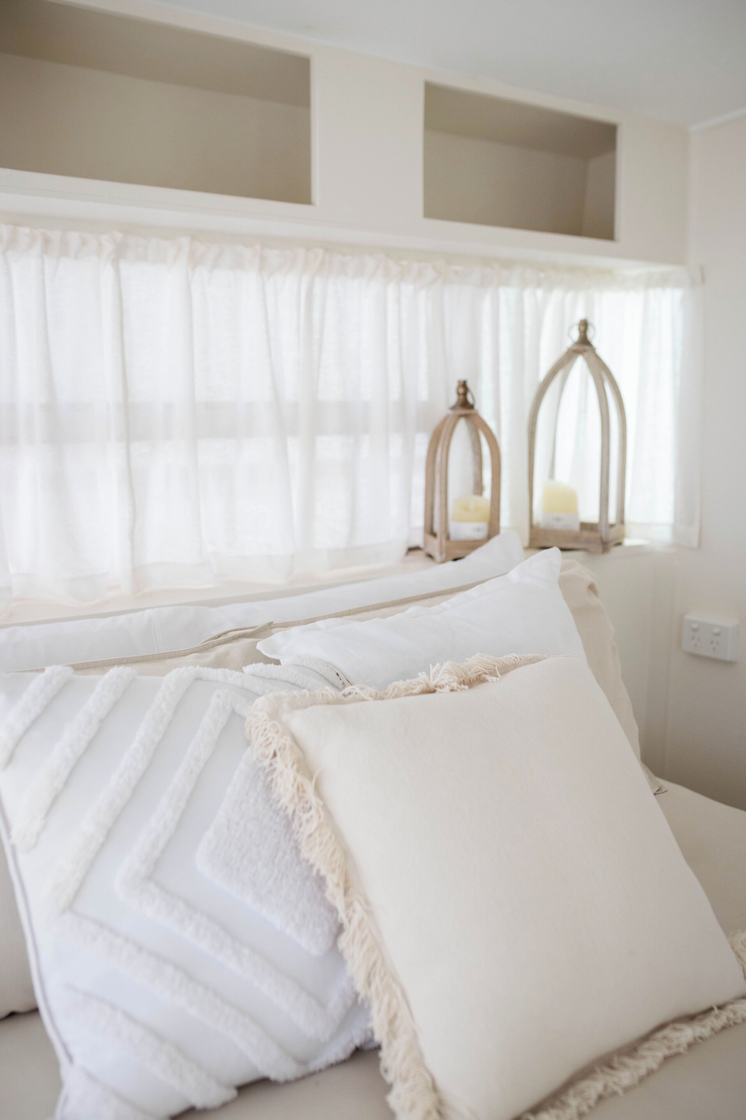 Une chambre à coucher avec un lit, du linge de lit blanc et deux lanternes fixées au mur.