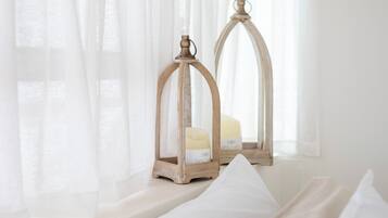 Un dormitorio con cama, cortinas blancas y dos faroles de madera en el alféizar de una ventana.