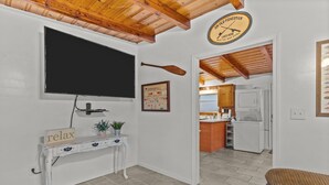 A living room with a television, a clock, a framed poster, a small table with a plant, and a couch. - Pool! Blocks away from beach. Dog-Friendly! (Oak Island)