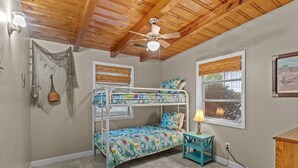 A bunk bed room with a ceiling fan, two windows with blinds, a small table with a lamp, and a wall-mounted shelf. - Pool! Blocks away from beach. Dog-Friendly! (Oak Island)