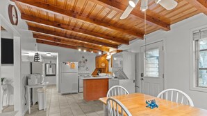 A modern kitchen with wooden beams, white appliances, and a dining area with a wooden table and white chairs. - Pool! Blocks away from beach. Dog-Friendly! (Oak Island)