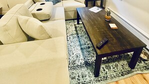 En stue med en hjørnesofa, et sofabord, et fjernsyn ophængt på væggen, et vindue med udsigt og en dør.