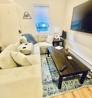 A living room with a sectional sofa, a coffee table, a TV mounted on the wall, a window with a view, and a door. - Adorable 1-bedroom condo in charming Telluride awaits you (Telluride)
