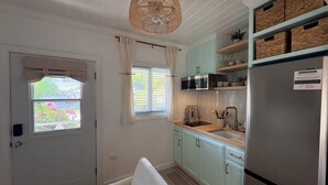 A kitchen with light green cabinets, a stainless steel refrigerator, a window with curtains, and a hanging light fixture.