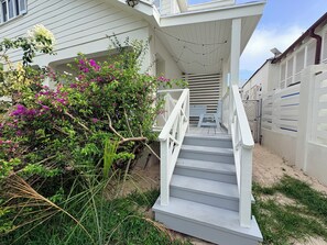 Uma escadaria branca leva a um alpendre coberto com um banco, cercado por vegetação e uma cerca.