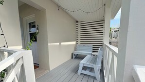 A covered porch with white railings, a bench, and a small table.