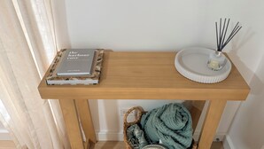 A wooden table with a guest book, a decorative tray, a scented candle, and a woven basket with a blanket.