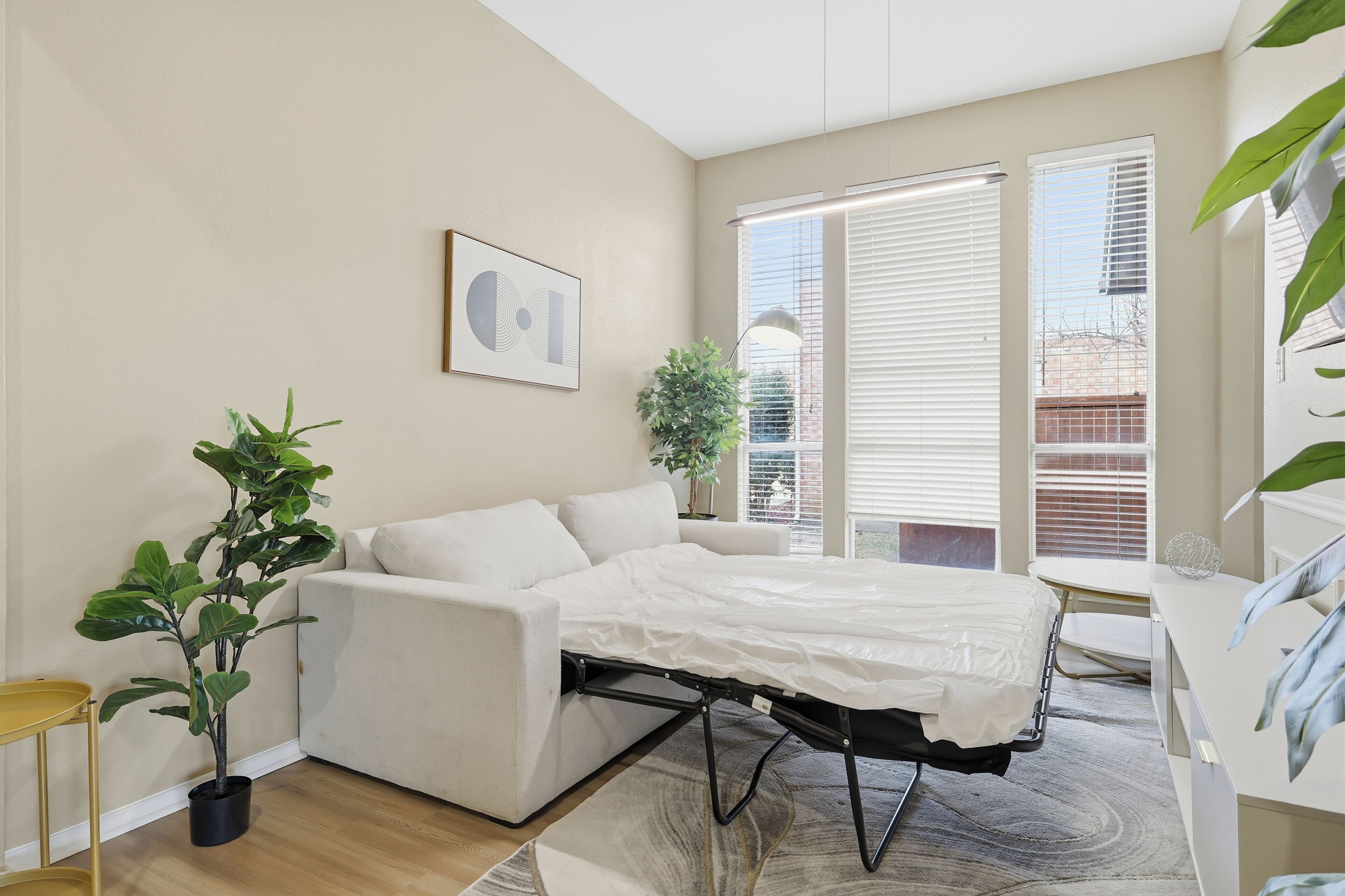 Un dormitorio moderno con sofá cama tipo futón, una planta en maceta y un amplio ventanal con persianas.