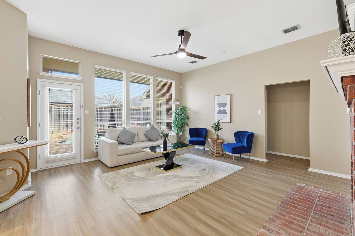 A spacious living room with a white sofa, blue chairs, a coffee table, and a ceiling fan.
