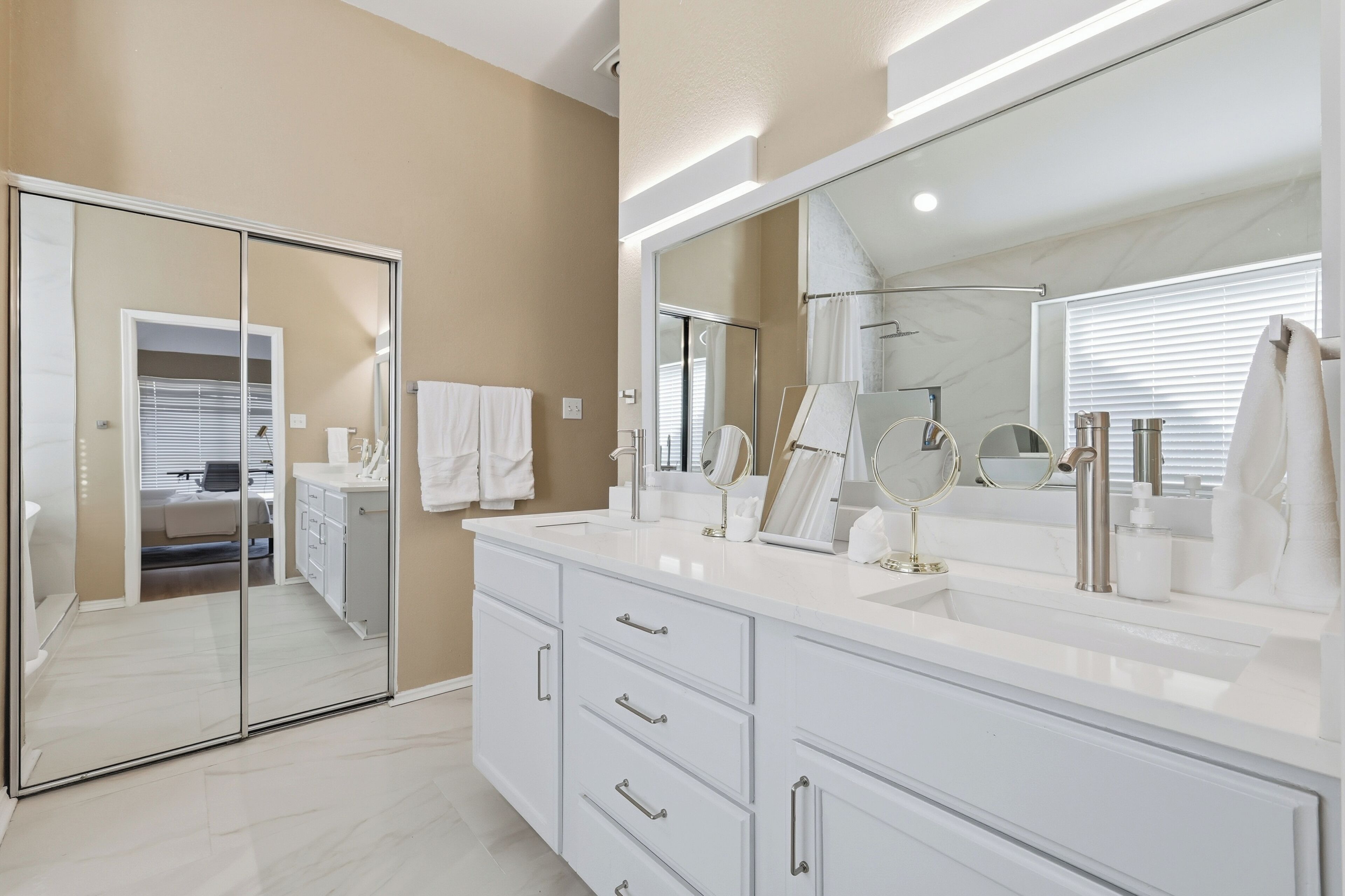 A modern bathroom with a large mirror, white vanity, and a walk-in closet.