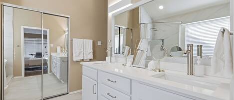 A modern bathroom with a large mirror, white vanity, and a walk-in closet.