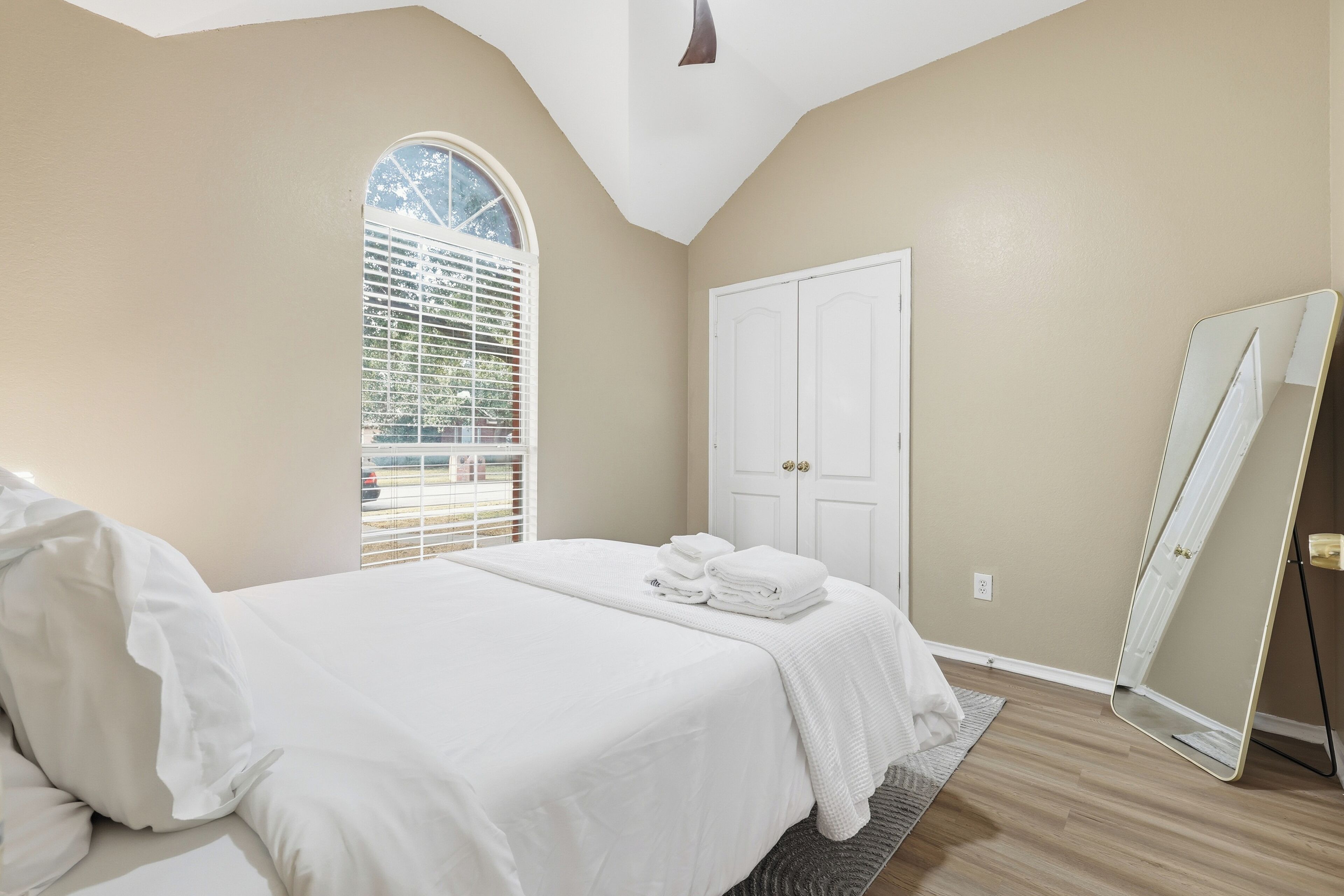 A bedroom with a bed, a window with blinds, a door, and a mirror.