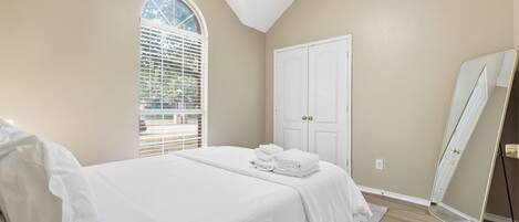 A bedroom with a bed, a window with blinds, a door, and a mirror.