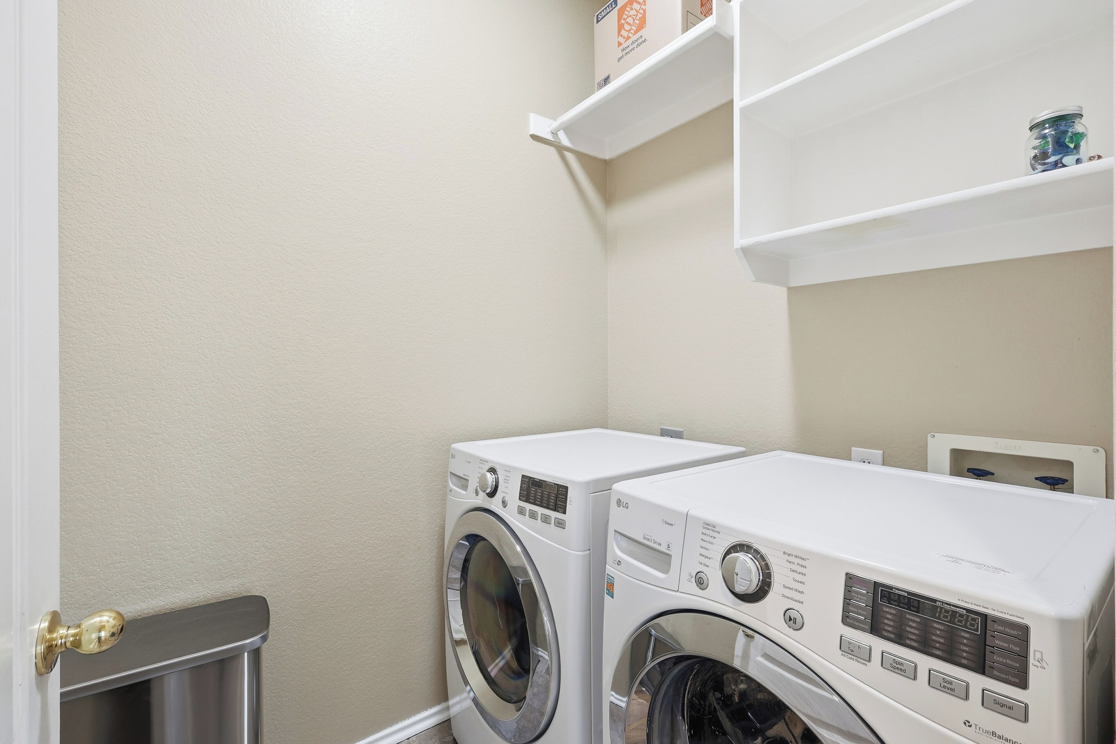 A laundry room with two front-loading washing machines and a small trash bin.