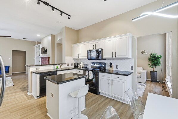 A modern kitchen with white cabinets, a central island, stainless steel appliances, and a dining area with a white table and chairs.