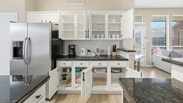 A modern kitchen with white cabinetry, a stainless steel refrigerator, and a granite countertop. - Modern 4B Retreat with Pool in Frisco (Frisco)