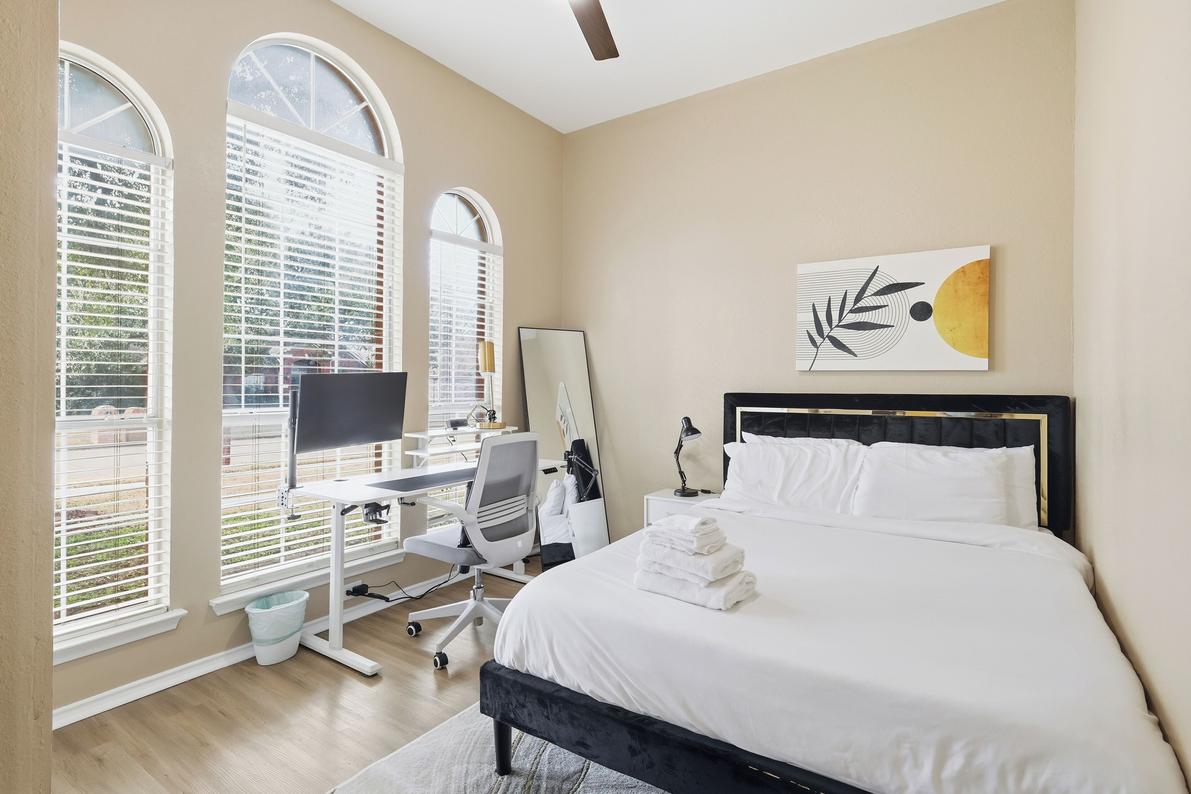 Une chambre à coucher avec un lit, un bureau, une chaise et une œuvre d’art accrochée au mur.