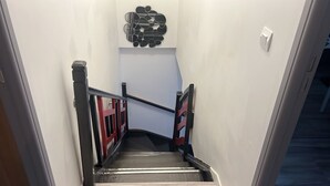 Una escalera con barandilla, una barrera de seguridad roja y negra, y un interruptor de luz fijado a la pared.