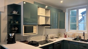 Una cocina moderna con gabinetes color turquesa, microondas integrado, cafetera y ventana con persianas.
