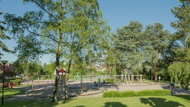 Un parque con juegos infantiles, bancos y árboles.