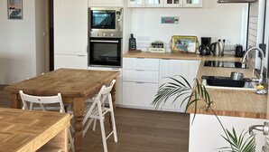 Una cocina compacta con armarios blancos, una mesa de comedor de madera y un horno empotrado.