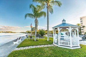 Un kiosque doté d’un toit bleu et de balustrades blanches, entouré de palmiers et offrant une vue sur le bord de l’eau.