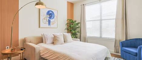 Un dormitorio moderno con una cama grande, un sillón azul, una lámpara de pie y un cuadro en la pared.