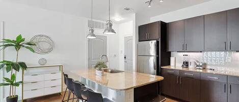 Una cocina moderna con armarios oscuros, electrodomésticos de acero inoxidable y una isla central con taburetes de bar.