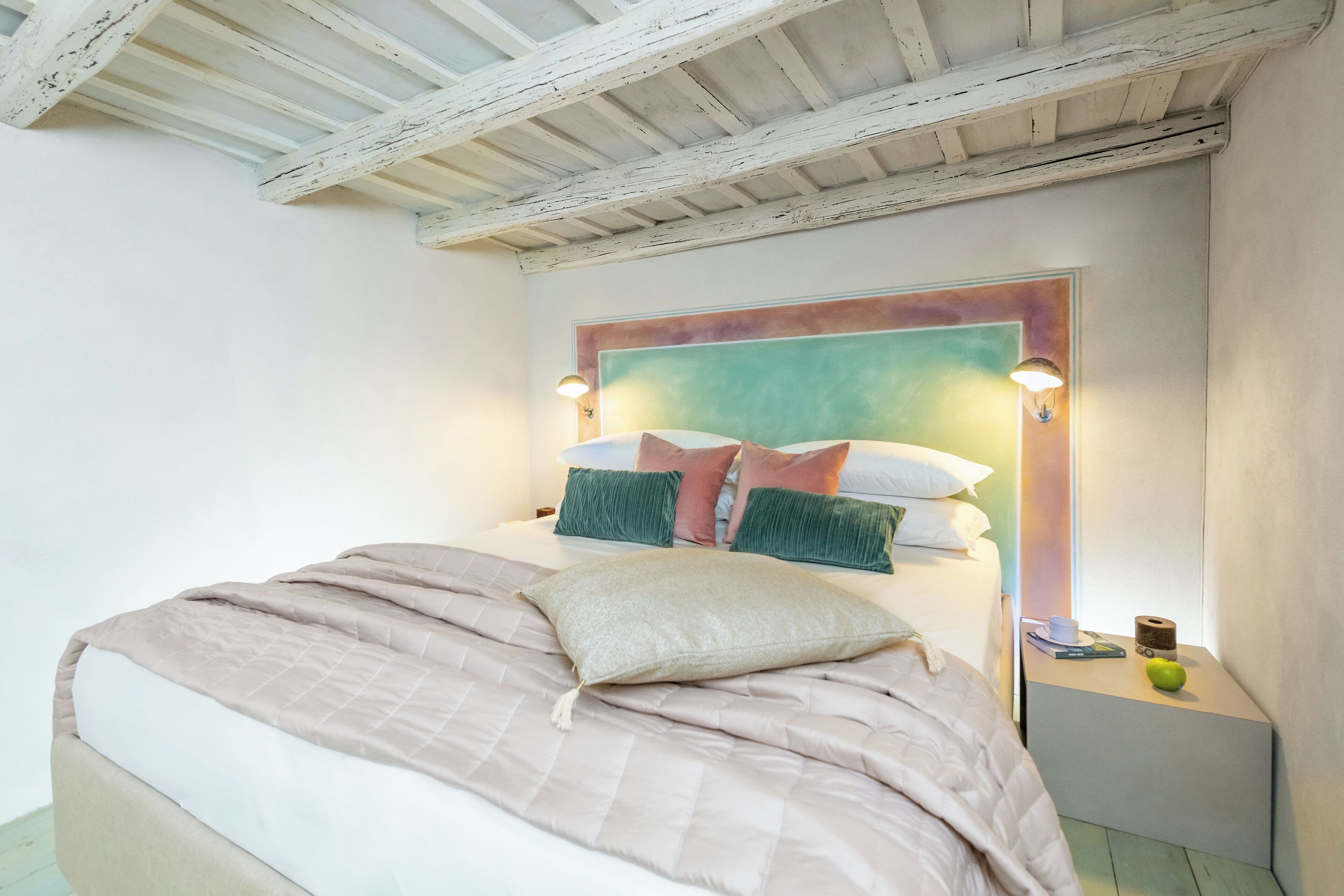 A bedroom with a bed, a headboard, bedside tables, and a wall-mounted light fixture.