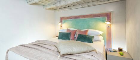 A bedroom with a bed, a headboard, bedside tables, and a wall-mounted light fixture.