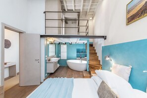 A modern bedroom with a large bed, a built-in bathtub, and a staircase leading to an upper level. - NEW! Spanish Steps Prestige Apartment (Roma)