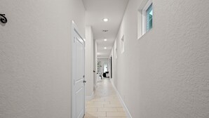 A narrow hallway with white walls, a tiled floor, and a door on the left. - Modern 3BR Near RiverWalk•Sleeps 8•Free Parking (San Antonio)