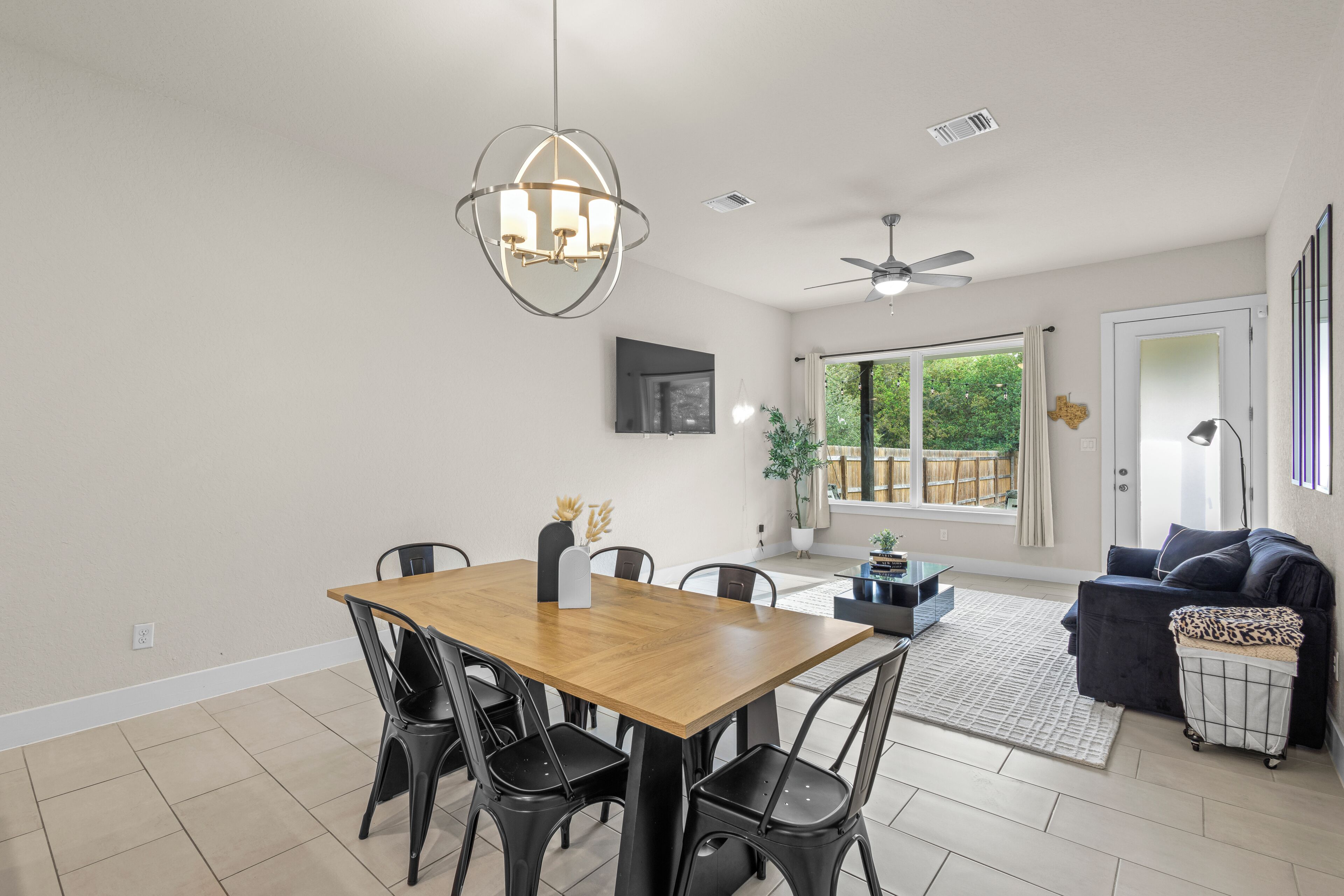 A dining area with a wooden table and black chairs, a ceiling fan, and a large window with a view of greenery.