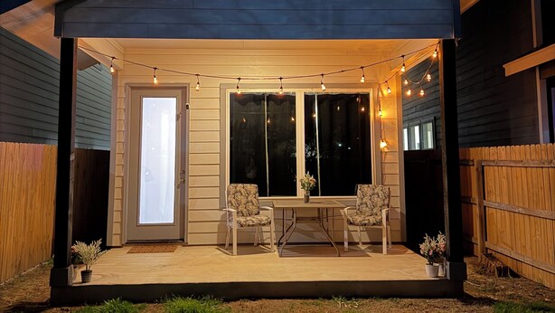 A covered patio area with two chairs and a table, a small potted plant, and string lights. - Modern 3BR Near RiverWalk•Sleeps 8•Free Parking (San Antonio)