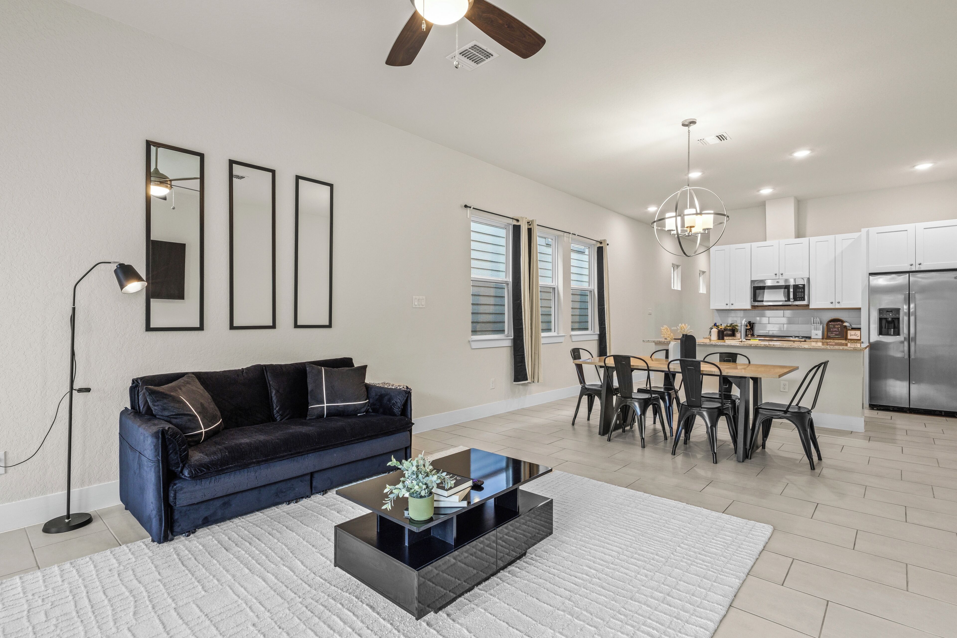 A modern living room with a black sofa, a glass coffee table, and a dining area with a wooden table and chairs.