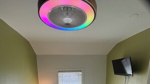Et soveværelse med seng, ventilator, fjernsyn, vindue og lampe.