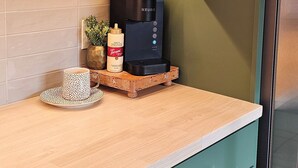 Uma cozinha com armários verde-água, bancada de madeira, cafeteira e uma xícara de café.