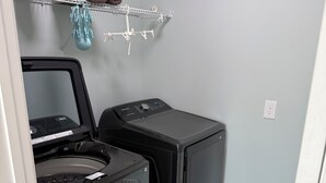 Une buanderie équipée de deux machines à laver à chargement frontal, d’un étendoir à linge et d’un paquet de lessive posé sur une étagère.