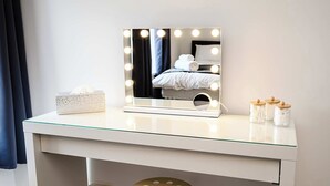 A vanity with a mirror, lights, a tissue box, and jars on a glass-topped dresser. - Ty Glyndwr by STAE-Homes (Trehafod)