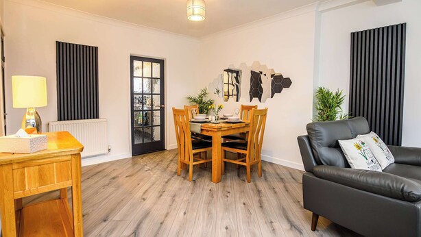A modern living room with a dining table, wooden chairs, a black leather sofa, and a radiator. - Ty Glyndwr by STAE-Homes (Trehafod)