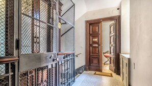 A hallway with a metal gate, a wooden door, and a chair. - Bright & Stylish 2 bed Apartment in Trastevere (Roma)