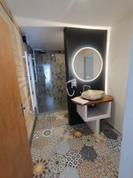 A bathroom with a wooden door, a white sink with a round mirror, and a patterned floor.