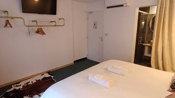 Habitación de hotel con cama, televisor montado, perchero y puerta que da a un baño.