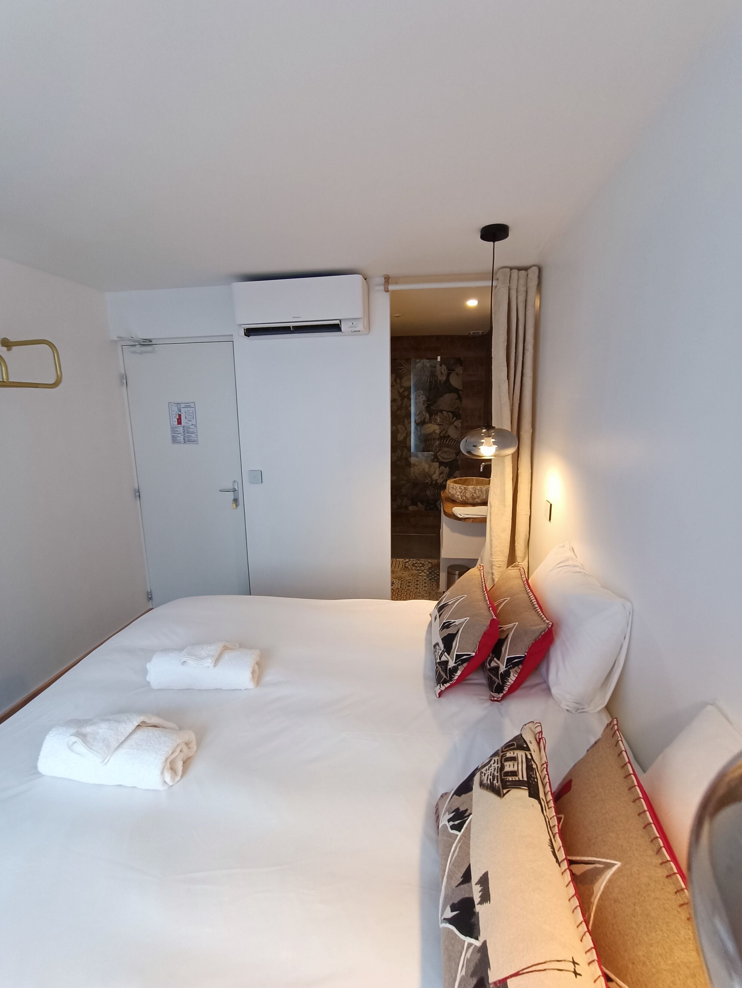 Ein Hotelzimmer mit Bett, Schrank, Klimaanlage, Badezimmer mit Dusche und Nachttisch mit Lampe.