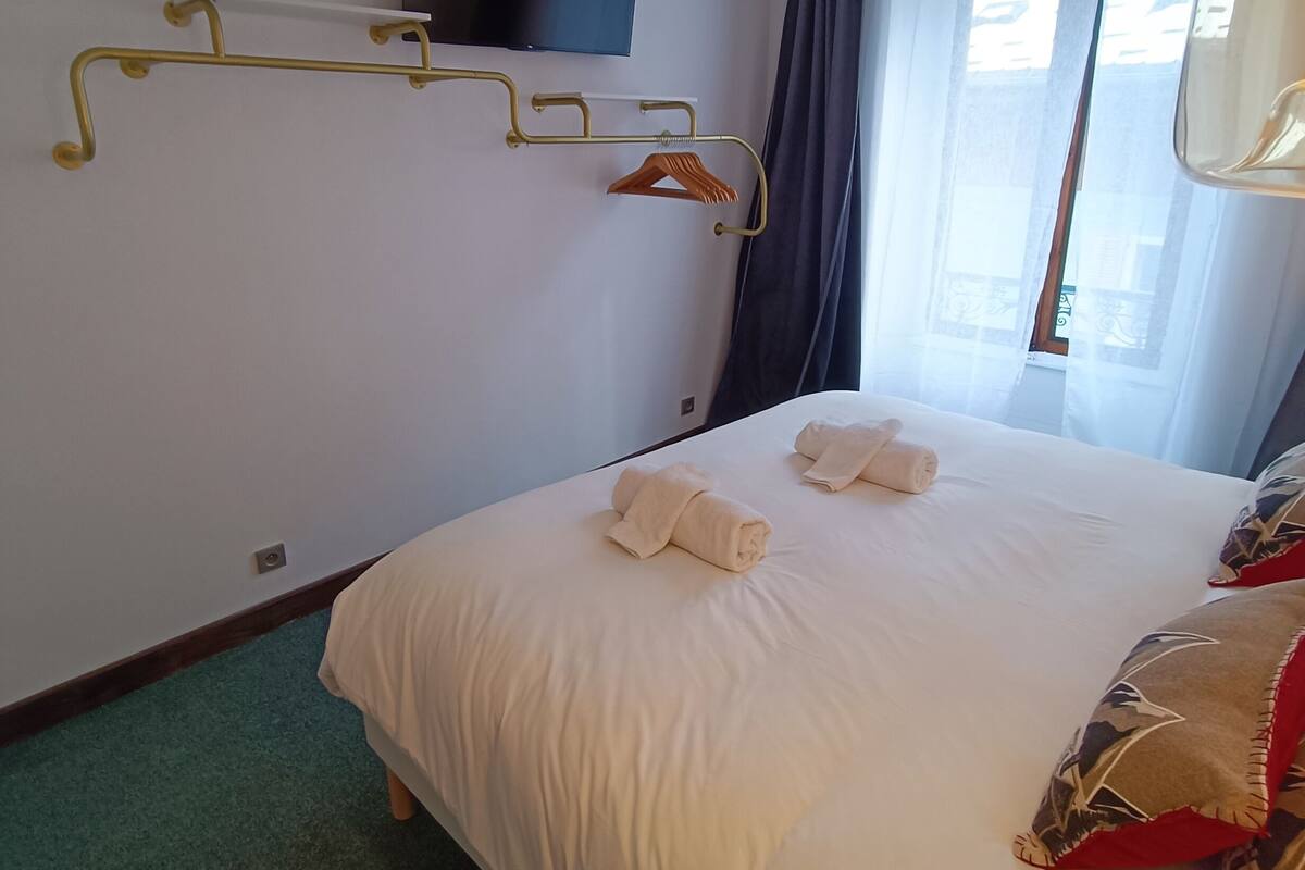 A hotel room with a large bed, a mounted TV, a coat rack, and a window with curtains.