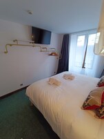 Une chambre d’hôtel avec un grand lit, un téléviseur fixé au mur, un porte-manteau et une fenêtre avec des rideaux.